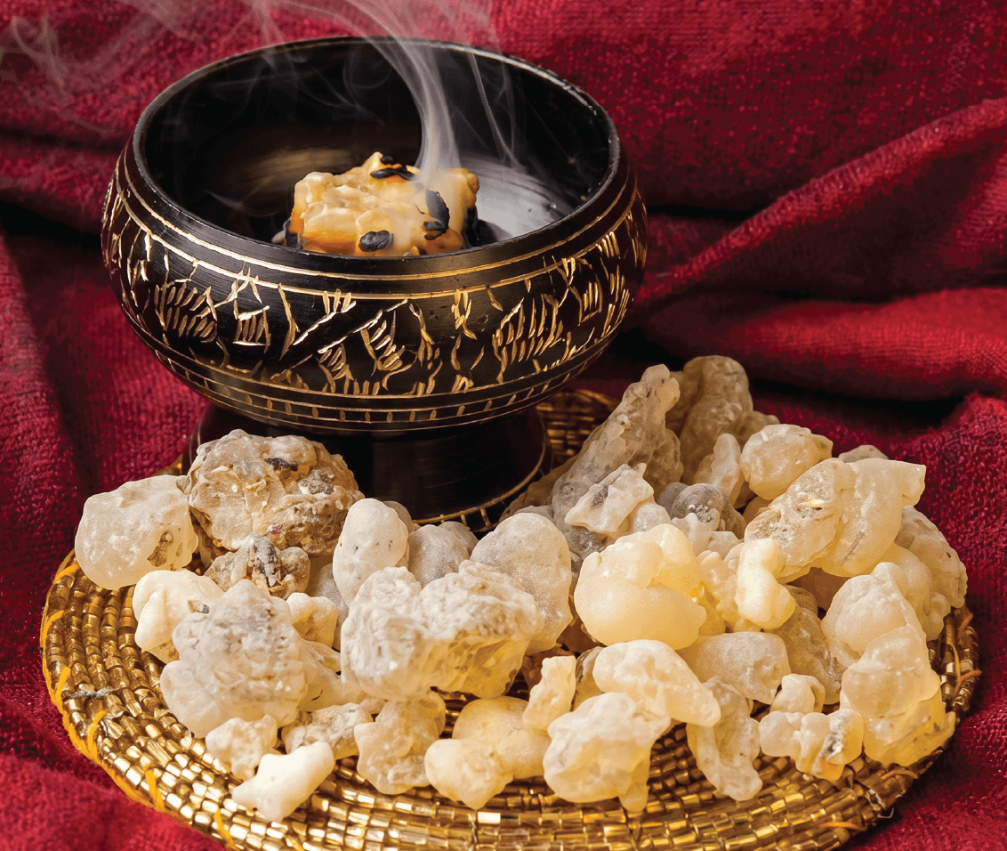 Resin being placed on a lit charcoal disc in a traditional burner, with smoke rising.